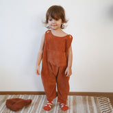 Toddler wearing terracotta baby corduroy overalls standing on rug